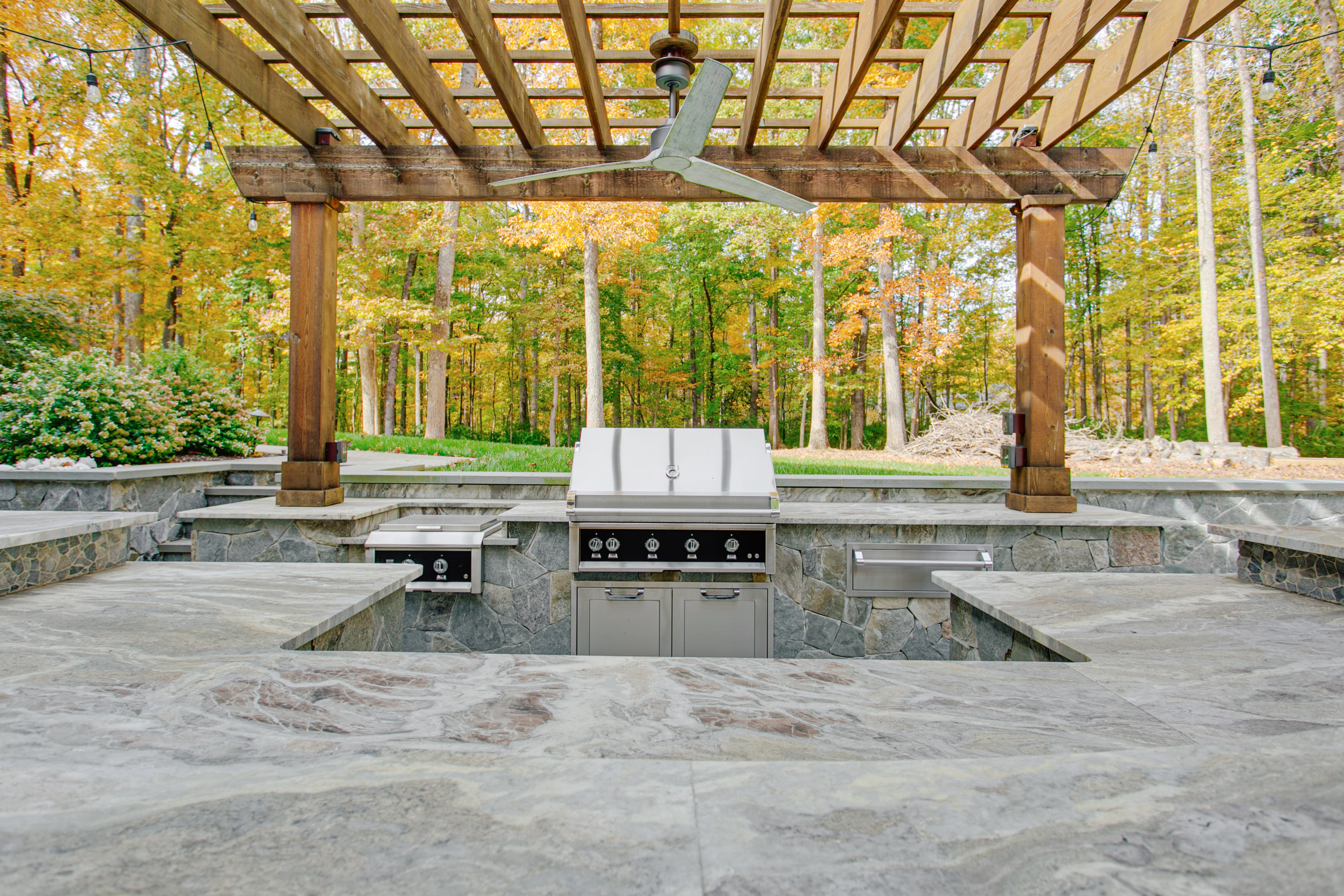 large backyard with stone 
        outdoor kitchen under wood pergola